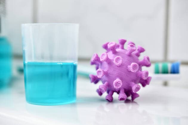Coronavirus-Miniatur neben einem Becher mit Mundwasser