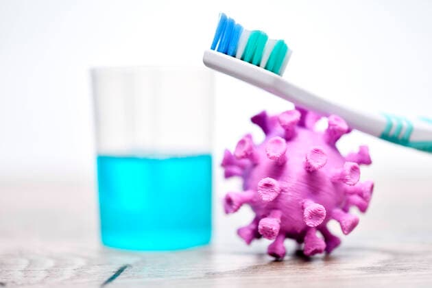 FOTOMONTAGE, Coronavirus-Miniatur neben einem Becher mit Mundwasser