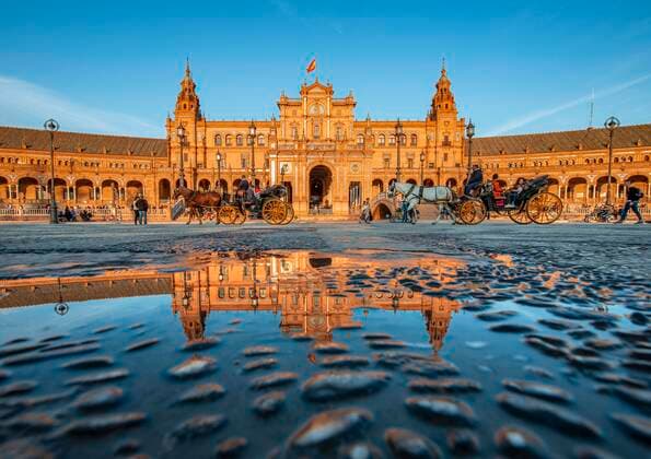 IMAGO Creative: Dichotomien, Reflexionen - Architektur  Hauptgebäude spiegelt sich in Wasserlacke, Plaza de Espana im Abendlicht mit Pferdektschen, Sevilla, Andalusien, Spanien, Europa *** Main building reflected in watercolours, Plaza de Espana in the evening light with horse carriages, Seville, Andalusia, Spain, Europe Copyright: imageBROKER/MaraxBrandl iblmab05799120.jpg