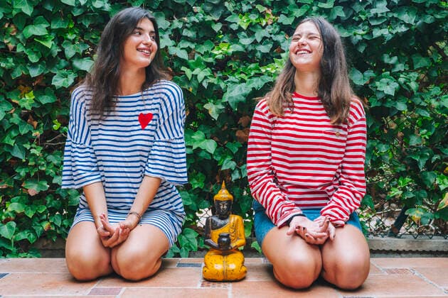 Smiling sisters meditating with Buddha sculpture in backyard model released Symbolfoto property released DLTSF01070