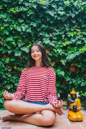 Smiling girl meditating by Buddha sculpture against plants in backyard model released Symbolfoto property released DLTSF01069