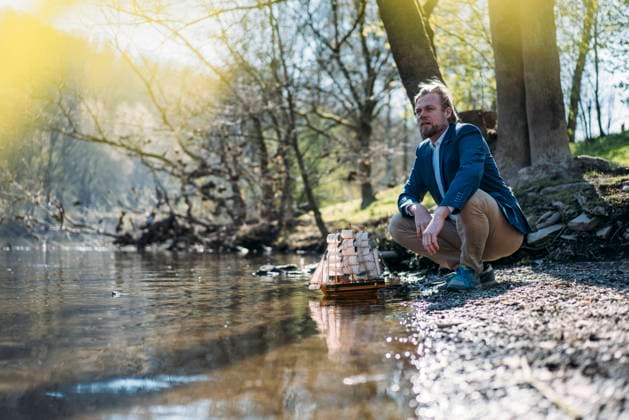 Male professional looking away while crouching by model boat at riverbank in park model released Symbolfoto JOSEF01469