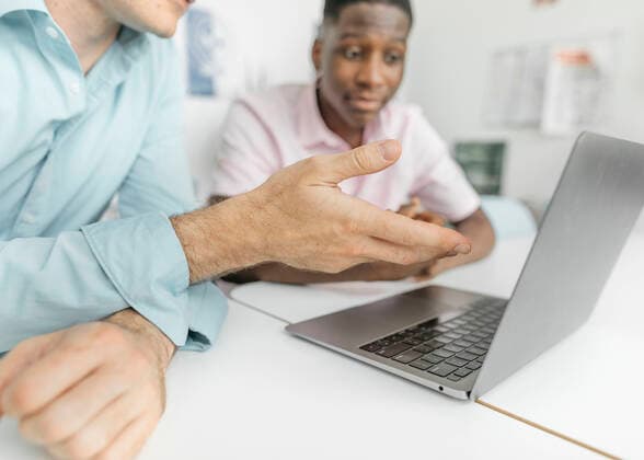 Colleagues working on laptop over table while sitting in office model released Symbolfoto property released KMKF01461