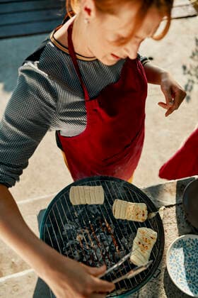 Woman preparing Halloumi cheese on barbecue grill ZEDF03565