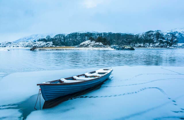 Blue boat in a frozen section of a lake in Killarney National Park with snow-covered trees in the background and low lying clouds; County Kerry, Ireland  Copyright: MichealxHoward 13491588