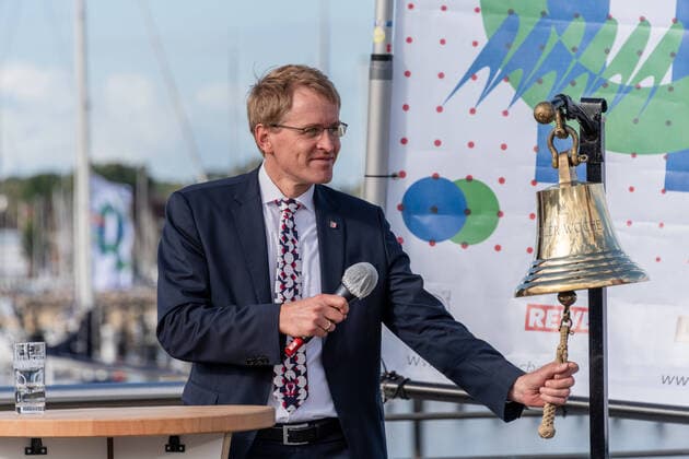 Die Kieler Woche 2020 (5. bis 13. September) geht neue Wege, auch bei der offiziellen Eröffnung. Statt wie gewohnt auf dem Rathausplatz vor Tausenden Zuschauer*innen fand sie diesmal im kleinen Kreis dort statt, wo das seglerische Herz der KiWo schlägt, im Olympiazentrum Schilksee. Heute um 16 Uhr wurde der Startschuss für das Segelereignis in Gegenwart von Landtagspräsident Klaus Schlie, Ministerpräsident Daniel Günther, Stadtpräsident Hans-Werner Tovar, Oberbürgermeister Ulf Kämpfer, Regatta-Organisationsleiter Dirk Ramhorst und Werner M. Dornscheidt, langjähriger Vorstand der Messe boot in Düsseldorf eröffnet. Das traditionelle Glasen mit der Schiffsglocke übernahm Ministerpräsident Daniel Günther, Werner M. Do