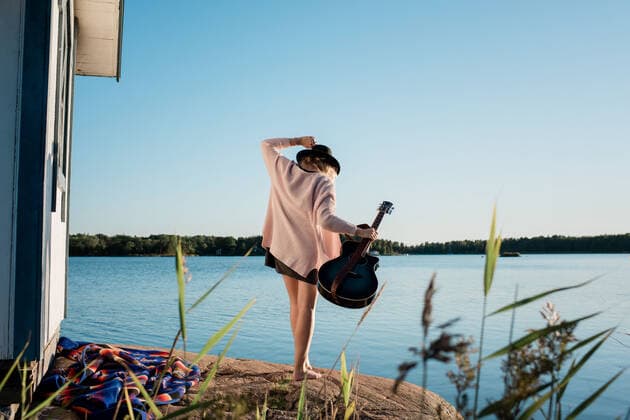 woman walking on a rock at the beach holding her guitar in the sun Norrtälje, Stockholm County, Sweden CR_RABE200909-494231-01 ,model released, Symbolfoto