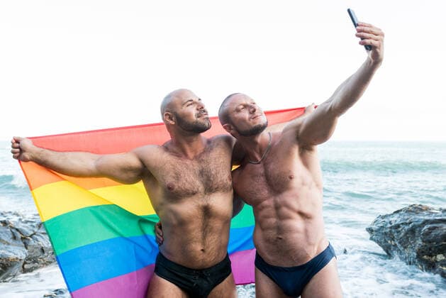 Lgbt pride concept. Gay bear couple holding rainbow flag with open arms taking a selfie photo. Benalmádena, AL, Spain CR_VZNFTC200908-480734-01 ,model released, Symbolfoto