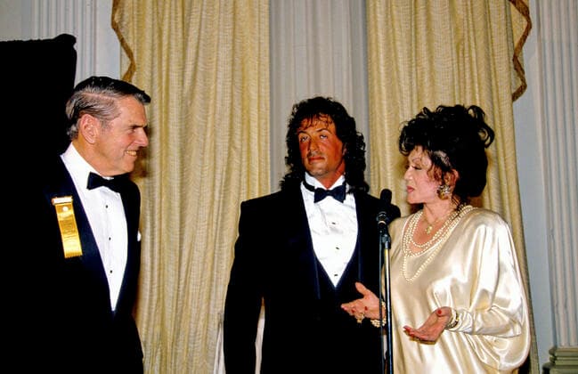 Jackie Stallone, right, mother of American actor, director, screenwriter, and producer Sylvester Stallone, center, makes remarks as her son is honored by the Washington, DC Touchdown Club in Washington, DC on January 23, 1988. At left is former Washington Redskins head coach George Allen. Copyright: x 1988,x2019xConsolidatedxNewsxPhotosxxxAllxRightsxReservedx