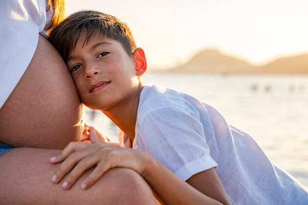 Son keeping head on pregnant mother s stomach while sitting at beach during sunset model released Symbolfoto DLTSF01140