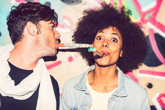 Close-up of carefree couple blowing party horns against wall at night model released Symbolfoto EHF00871