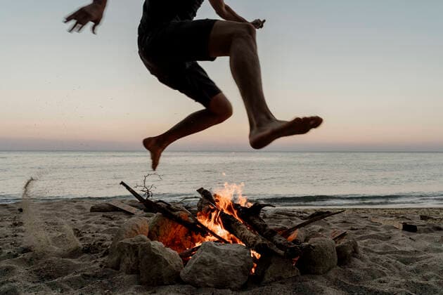 IMAGO Creative: Klimawandel - Nachhaltiges Reisen Man jumping over campfire at beach during sunset model released Symbolfoto AFVF07232