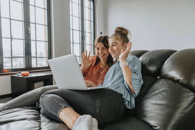 Friends waving while video conferencing over laptop on sofa at home model released Symbolfoto property released MFF06109