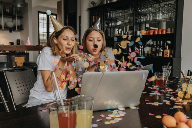 Geburtstag - Symbolbilder Creative Highlights Symbolfotos Cheerful friends blowing confetti while video conferencing over laptop while sitting at home model released Symbolfoto property released MFF06140