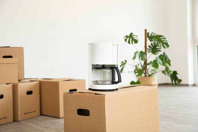 IMAGO Creative: Haushaltsgeräte - Kaffeemaschine Coffee machine on cardboard box against white wall in new house property released MJFKF00545