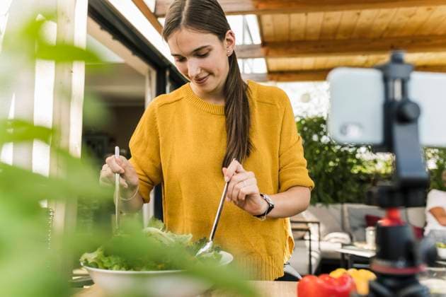 IMAGO Creative: Veganuary, fleischlos leben Smiling young woman filming with smart phone while preparing food at home model released Symbolfoto property released UUF21047