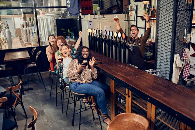 Excited female friends sitting at the counter in a pub watching Tv model released Symbolfoto property released ZEDF03654