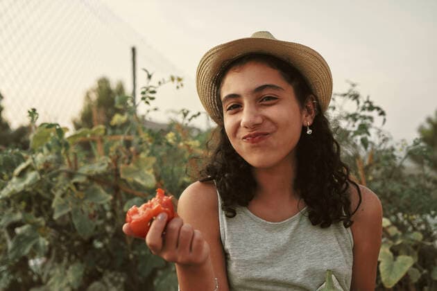 A girl with curly hair is eating a tomato in her own garden Jaén, AL, Spain CR_NNSU201014C-522903-01 ,model released, Symbolfoto