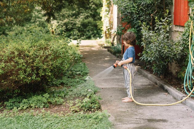 Boy watering plants while standing on footpath at back yard model released Symbolfoto ALBF01570
