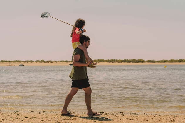 IMAGO Creative: Klimawandel - Umwelterziehung Father carrying daughter on shoulders while walking at beach against clear sky during sunny day model released Symbolfoto ERRF04424