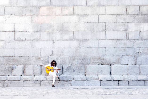 IMAGO Creative: Momentaufnahmen Flamenco guitarist playing guitar while sitting on bench against concrete wall model released Symbolfoto JCMF01398