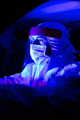 IMAGO Creative: 2022 Farbe des Jahres: Very Peri, Veilchenblau Man wearing protective suit driving illuminated ambulance at night model released Symbolfoto JCMF01421