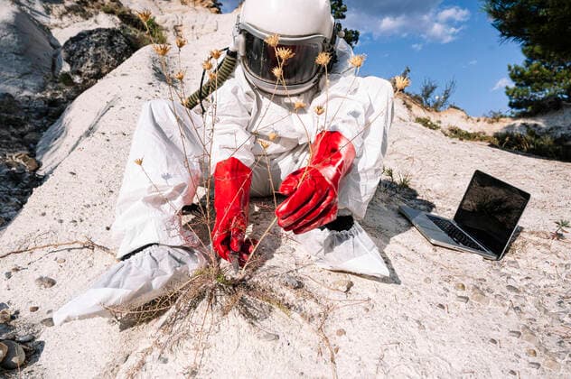 IMAGO Creative: 2021 Favoriten IMAGO Creative: Klimawandel - Zukunft und Innovation Male astronaut picking plant while sitting with laptop on mountain model released Symbolfoto JCMF01431