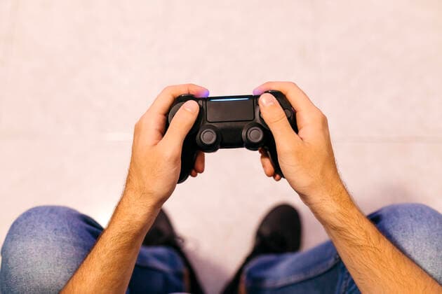 IMAGO Creative, Lifestyle, Gaming Young male gamer holding controller while playing at home model released Symbolfoto property released JRFF04749