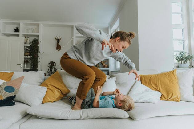 Mother gesturing while standing on sofa by boy at home model released Symbolfoto property released MFF06217