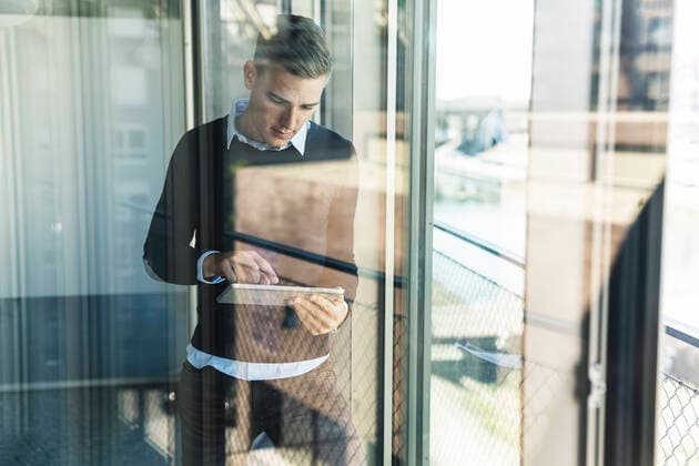 Male professional working over digital tablet while standing in office seen through window model released Symbolfoto property released UUF21524