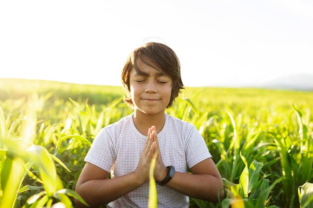 Smiling boy practicing yoga while sitting on grass in meadow model released Symbolfoto VABF03551