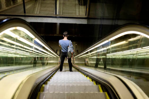 IMAGO Creative: Corporate: Klimaschutz, Digitalisierung und Urbanisierung Young man with backpack standing on illuminated escalator at subway model released Symbolfoto VABF03595
