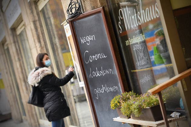Themenbild: Coronavirus Pandemie Folgen fuer die Gastronomie. Eine Junge Frau steht mit Mundschutz,Maske vor einer verschlossenen Tuere eines Wirtshauses neben einem Schild: WEGEN CORONA LOCKDOWN GESCHLOSSEN, Geschlossenes bayerisches Restaurant am Sendlinger Tor in Muenchen. Seit dem 2.November muss wegen dem Lockdown light die Gastronomie geschlossen bleiben, Schliessung-Folge der Corona Pandemie,Lockdown,Shutdown,Inzidenzwert. MODEL RELEASED!