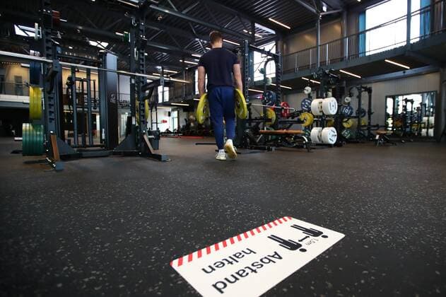 Diez Fitnessstudios in der Corona-Zeit Hinweis Abstand halten auf dem Boden eines Fitnessstudios, dahinter ein Mann mit Hantelscheiben Fitnessstudios in der Corona-Zeit Copyright: xEibner-Pressefotox EP_RWS