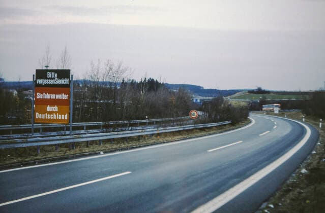 Hinweisschild BITTE VERGESSEN SIE NICHT: SIE FAHREN WEITER DURCH DEUTSCHLAND vor dem Grenzübergang Rudolphstein Hirschberg, einem der wenigen für Kraftfahrzeuge passierbaren Grenzübergänge, Innerdeutsche Grenze DDR Deutsche Demokratische Republik BRD Bundesrepublik Deutschland, an der Autobahn 9 zwischen Rudolphstein (Oberfranken Bayern) und Hirschberg (Bezirk Gera, heute Thüringen)