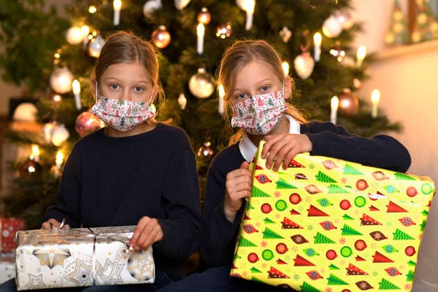 24.11.2020, (Modelreleased). Symbolbild, Eine Familie im Allgäu sitzt am Heiligen Abend vor dem Weihnachtsbaum im Wohnzimmer, Zwei Geschwisterkinder mit Mund-Nasen-Schutzmaske warten auf die Bescherung. Kontaktverbote und Ausgangsbeschränkungen machen der Bevölkerung zur Corona-Zeit das Leben schwer, die gewohnten Treffen unter den Familien sind dieses Jahr wegen der Pandemiebeschränkungen nur Eingeschränkt möglich. 24.11.2020, Familie feiert Weihnachten mit Corona-Einschränkungen 24.11.2020, Familie feiert Weihnachten mit Corona-Einschränkungen