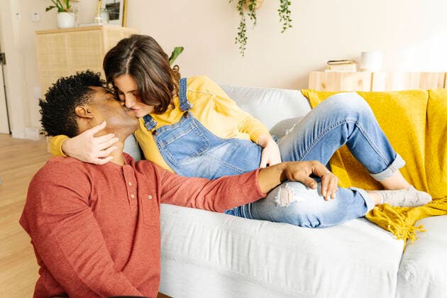 Husband kissing his pregnant wife on a sofa. Interracial couple concept Sant Cugat del Vallès, CT, Spain CR_KTUU201128-569151-01 ,model released, Symbolfoto ,property released