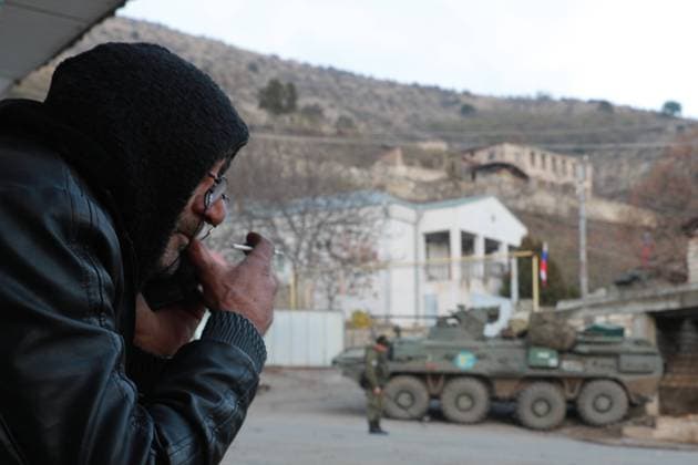 LACHIN, AZERBAIJAN - DECEMBER 1, 2020: A local man smoking against the background of Russian peackeepers in the town of Lachin (Berdzor). According to the trilateral agreement on a complete ceasefire signed by the leaders of Armenia, Russia, and Azerbaijan on 9 November, the town of Lachin was transferred to Azerbaijan on 1 December. Russian outposts are established along the contact line in Nagorno-Karabakh and the Lachin Corridor mountain pass. Alexander Ryumin TASS  TS0F0277