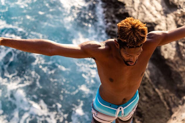 black cliff diver prepares to jump backwards of sea cliff into ocean Honolulu, HI, United States CR_ALKA201201-289363-01 EDITORIAL USE ONLY