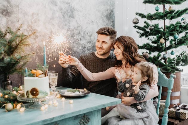Young family with a daughter in festive outfits at a served table with candles, garlands, sparklers and a cake near the Christmas tree on New Years Eve Russia, ??, Russia CR_MRZFGZ201208-582870-01 ,model released, Symbolfoto