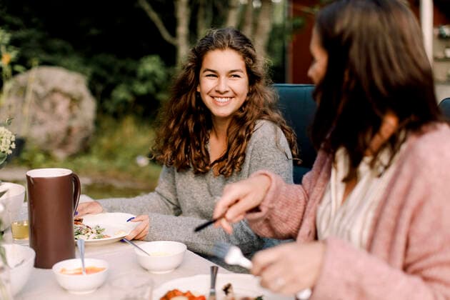 IMAGO Creative: Internationaler Frauenmonat, Gesundheit, Frauen in der Menopause Smiling woman talking to daughter while sitting by dining table in backyard, MA82714, Sweden, Stockholm Archipelago, model released, property released Copyright: xMaskotx