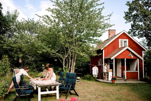 Mother and daughter preparing dining table in yard while father standing by house, MA82769, Sweden, Stockholm Archipelago, model released, property released Copyright: xMaskotx