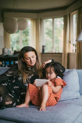 IMAGO Creative: Mutterschaft Mother looking at down syndrome daughter using mobile phone while sitting on sofa in living room, MA83030, Sweden, Stockholm, model released, property released Copyright: xMaskotx