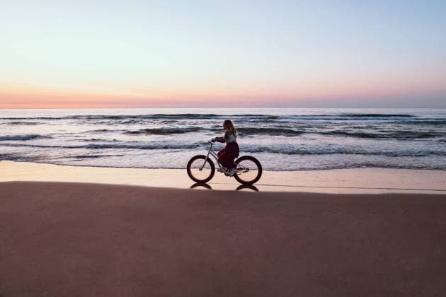 IMAGO Creative: Welttag f?r psychische Gesundheit am 10. Oktober Joyful woman riding bicycle along peaceful beach, Model released, Property released Copyright: xAdrianxSavax MR