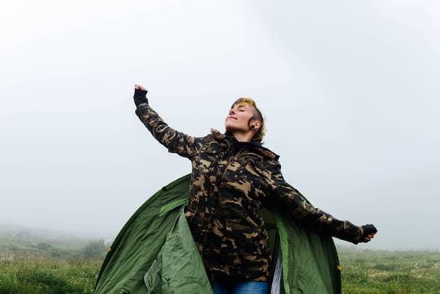 IMAGO Creative: Klimawandel - Nachhaltiges Reisen Positive female in warm clothes getting out of camping tent and stretching body during foggy morning in nature, Model released Copyright: xAlbertoxMenendezx MR