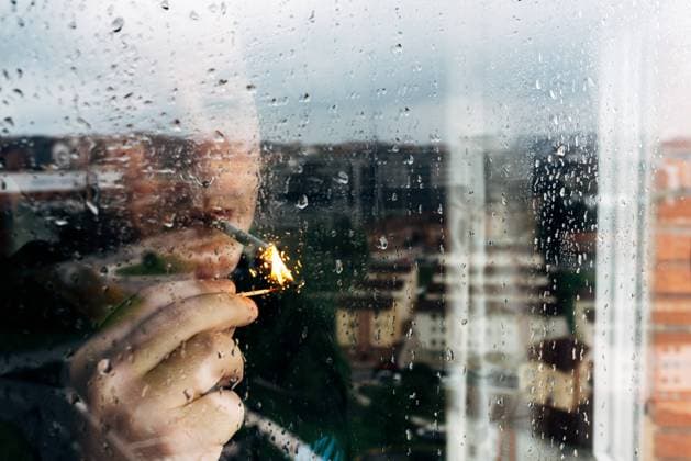 IMAGO Creative: Dichotomien, Reflexionen Unrecognizable male lighting cigarette with match while standing near wet window in rainy weather and spending day alone at home during quarantine because of coronavirus Copyright: xAlbertoxMenendezx Model Released