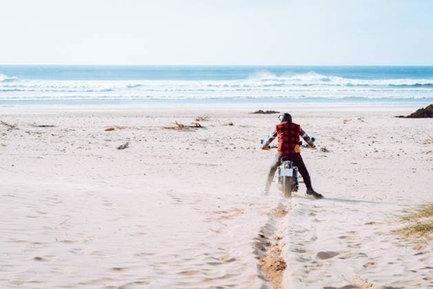 Back view of man sitting on motorcycle while exploring sandy beach with majestic ocean view, Model released Copyright: xAlbertoxMenendezx MR