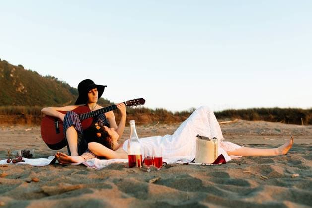 IMAGO Creative: Pride Month, Juni 2022, P?rchen und Familien Talented female musician playing acoustic guitar for girlfriend during picnic at seaside at sunset, Model released Copyright: xAlbertoxMenendezx MR