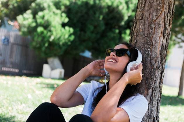 Peaceful woman in sunglasses and headphone listening to music while sitting on grass in park, Model released Copyright: xAlexandraxCoelhox MR