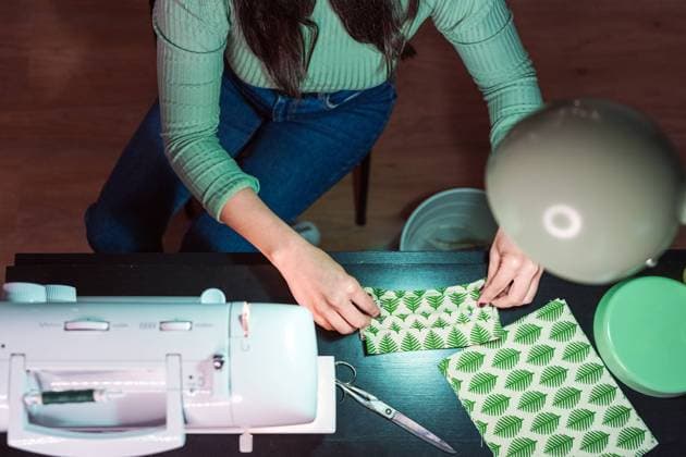 Cropped unrecognizable female tailor sitting in table making face masks near modern sewing machine in loft style atelier, Model released, Property released Copyright: xAlvaroxSanchezx MR